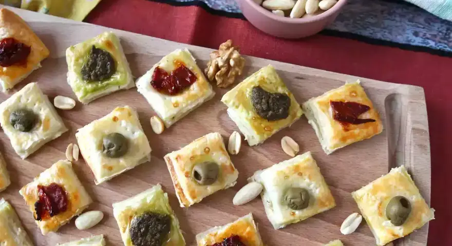 Sfiziose ricette con pasta sfoglia: quadratini dorati con olive, pesto e pomodori secchi, perfetti per un aperitivo.