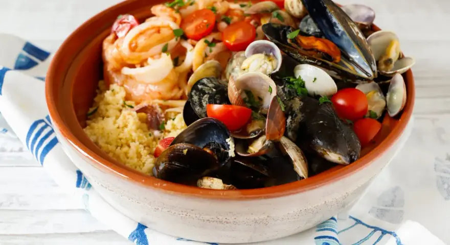 Un invitante cous cous di pesce, ricco di cozze, vongole, gamberi e pomodorini, guarnito con prezzemolo fresco.