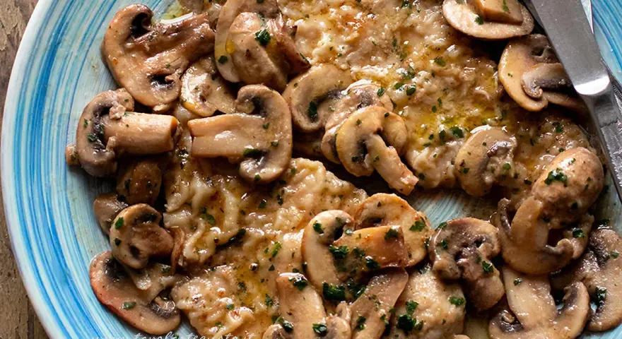 Scaloppine ai funghi, un piatto succulento con fettine di carne dorate e funghi champignon trifolati, guarnito con prezzemolo fresco.