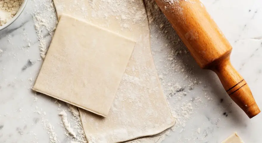Farinata e mattarello su piano di marmo, pronti per creare pasta sfoglia fatta in casa.