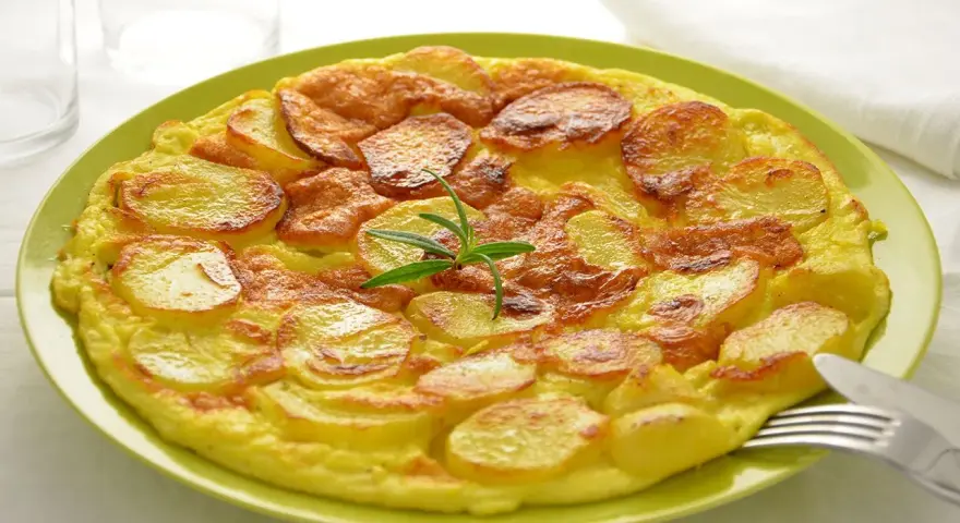 Frittata di patate dorata e gustosa, guarnita con rosmarino fresco, servita su un piatto verde.