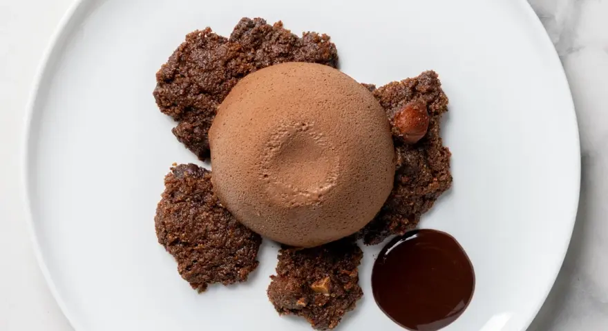 Semifreddo al cioccolato su croccanti biscotti al cacao, con una nocciola intera e una goccia di salsa al cioccolato.