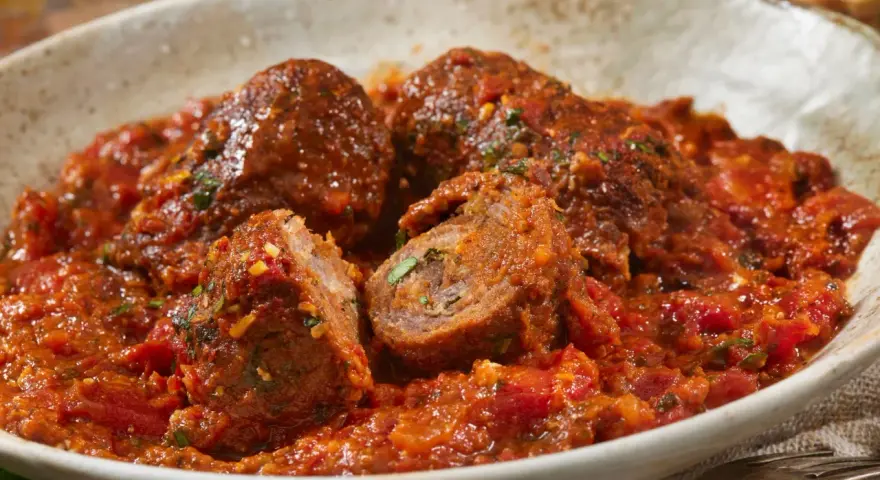 Involtini alla romana succulenti in un ricco sugo di pomodoro, con un interno visibile che rivela erbe aromatiche.