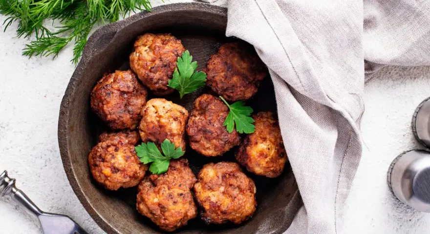 Polpette senza uova dorate in padella, guarnite con prezzemolo fresco. Un piatto gustoso e leggero, pronto per essere gustato.