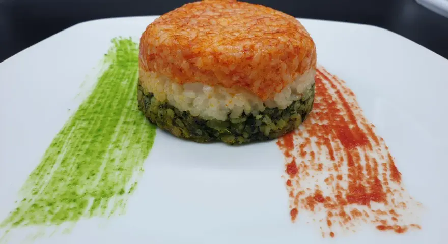 Un colorato timballo di riso a tre strati, con salse verdi e rosse che ricordano i colori di una bandiera.