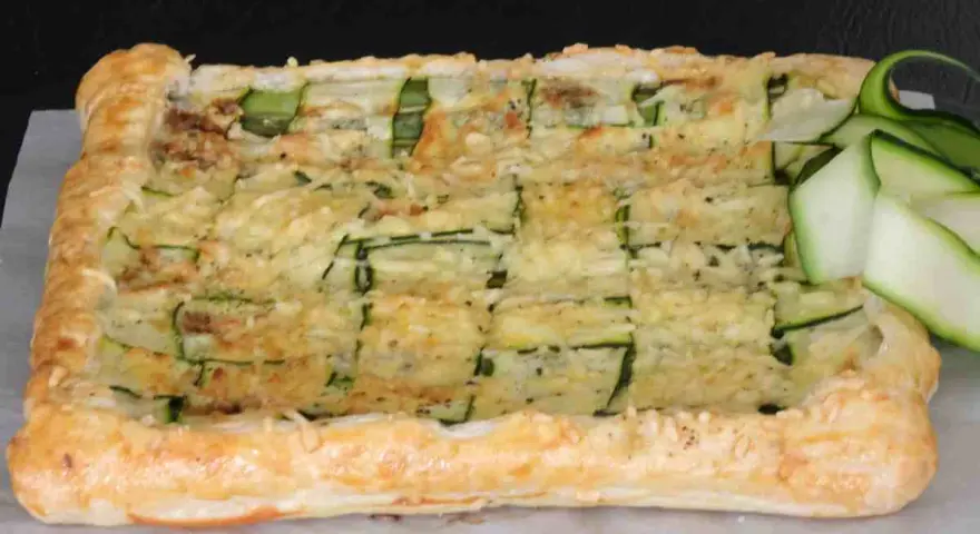 Torta salata con pasta sfoglia e zucchine a griglia, ricoperta di formaggio fuso e guarnita con fettine di zucchina fresca.