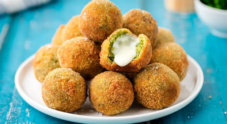 Pile di polpette di broccoli dorate e croccanti, una con il cuore filante di formaggio.