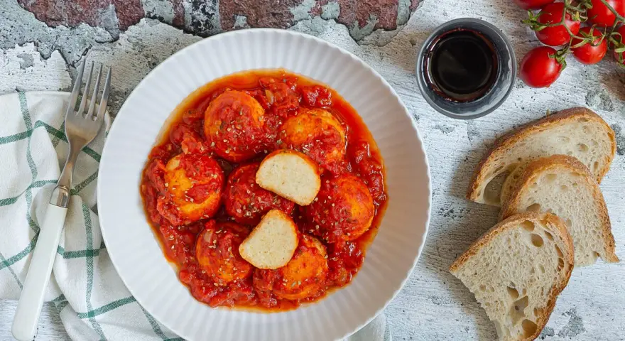 Polpette di ricotta al sugo, morbide e saporite, servite con pane casereccio e pomodorini freschi.