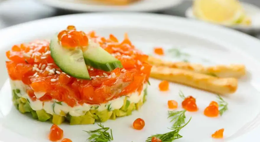 Tartare di salmone e avocado, un'idea per antipasti velocissimi senza cottura, guarnita con uova di pesce e cetriolo.