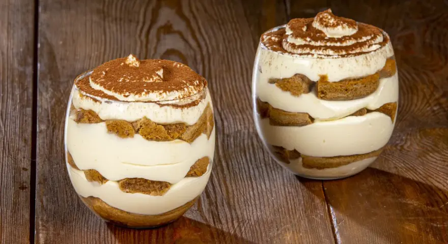 Due bicchieri di delizioso tiramisù senza uova, con strati di savoiardi e crema, spolverati di cacao.