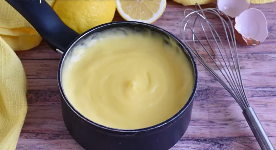 Crema pasticcera con amido di mais, liscia e vellutata, pronta per farcire dolci. Accanto, limoni, frusta e gusci d'uovo.