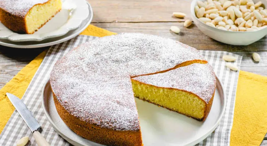 Torta soffice con farina di mandorle, spolverata di zucchero a velo. Un pezzo è già stato tagliato, pronto per essere gustato.