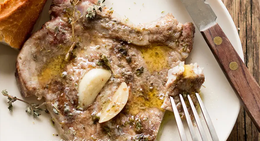 Succulente braciole di maiale cotte con aglio e erbe aromatiche, servite con pane croccante.