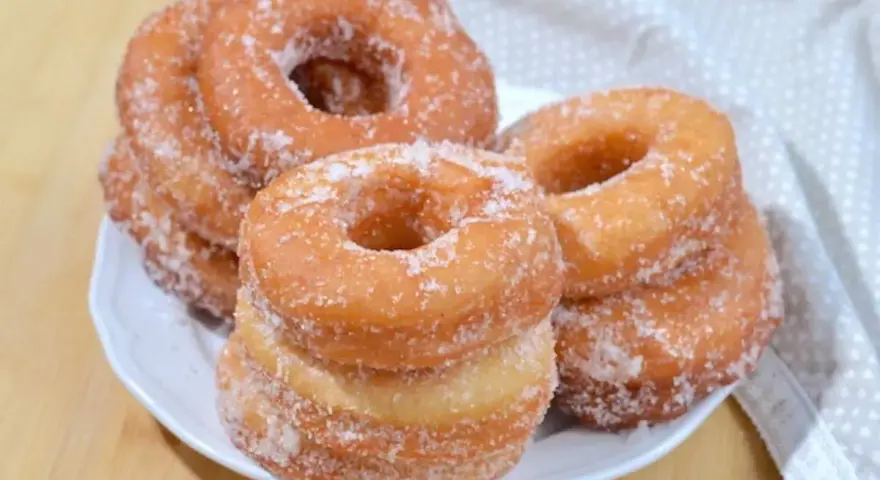 Ciambelle fritte dorate, cosparse di zucchero, pronte per essere gustate. Una deliziosa ricetta ciambelle fritte per ogni occasione.