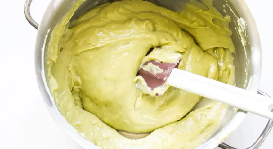 Una spatola mescola una densa crema al pistacchio in una ciotola d'acciaio.
