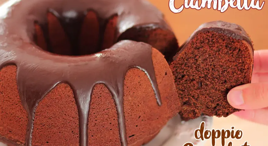 Ciambellone al cioccolato con glassa fondente. Una fetta viene sollevata, mostrando la consistenza soffice e il ricco colore del dolce.