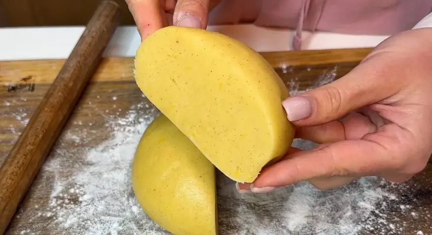 Mani che tengono un impasto giallo, profumato alla vaniglia, pronto per diventare una deliziosa pasta frolla senza burro.