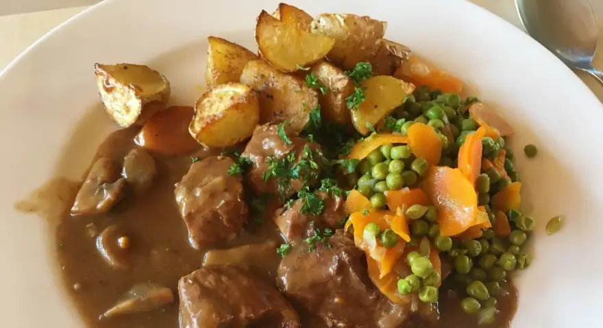 Un saporito spezzatino con piselli, carote e patate arrosto, guarnito con prezzemolo fresco.