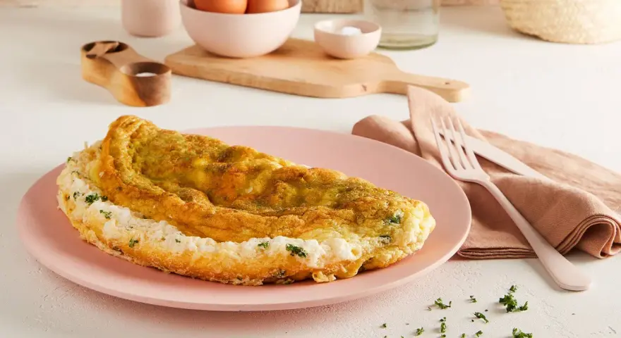Frittata soffice e dorata, preparata in friggitrice ad aria, servita su un piatto rosa con erbe fresche.