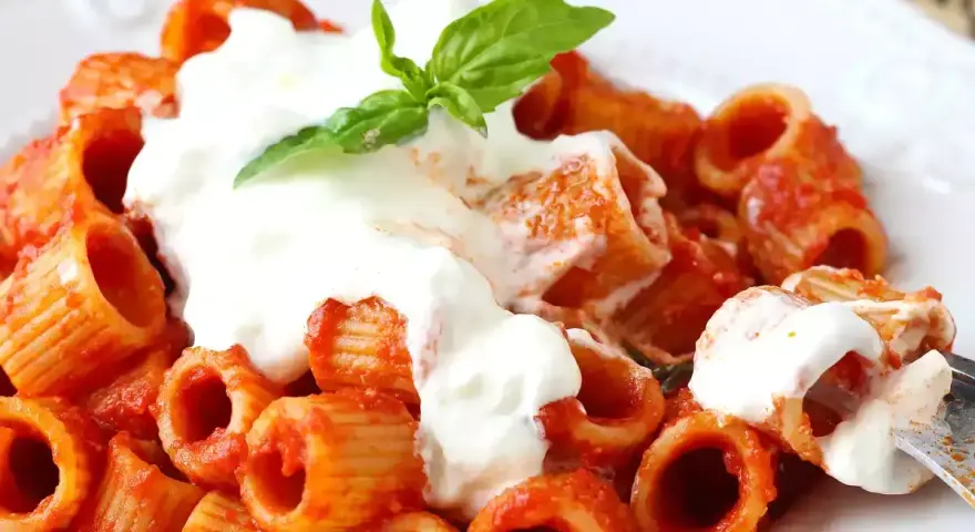 Rigatoni al sugo rosso con abbondante stracciatella cremosa e una fogliolina di basilico.