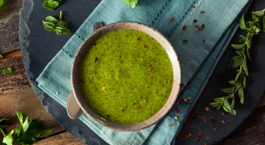 Una ciotola di vibrante salsa verde senza uovo, guarnita con peperoncino rosso tritato e erbe fresche. Perfetta per accompagnare i tuoi piatti preferiti.