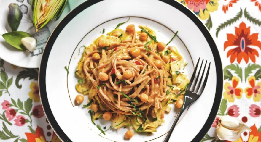 Un piatto invitante di pasta con carciofi alla siciliana, arricchito da ceci e erbe fresche, su un tovagliolo fiorito.