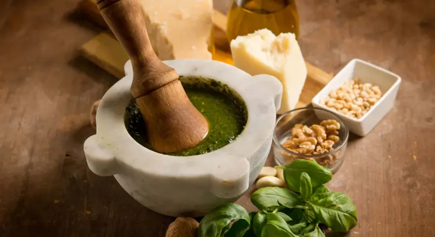 Mortaiolo in marmo con pestello in legno, basilico fresco, pinoli, noci, aglio, parmigiano e olio d'oliva, ingredienti per un autentico pesto di basilico.