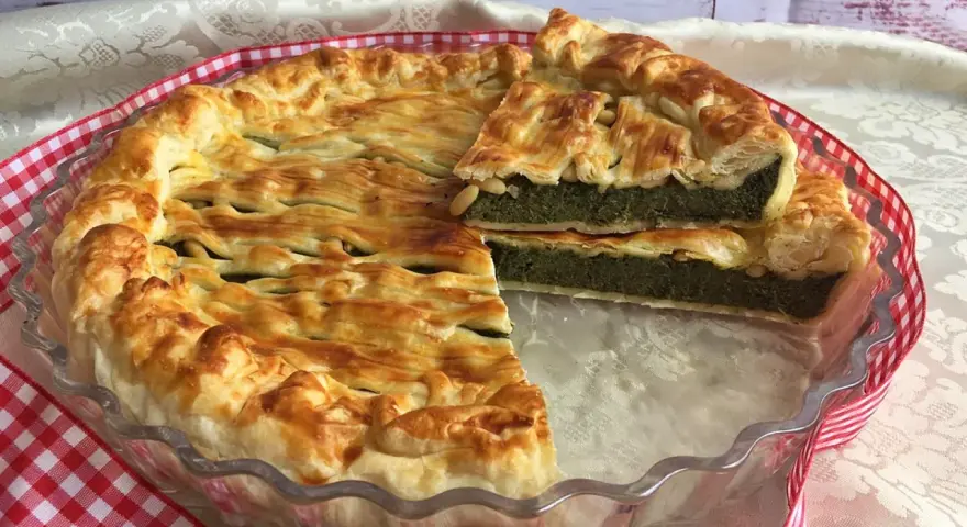 Torta salata ricotta e spinaci dorata e invitante, con una fetta tagliata che mostra il ripieno verde e cremoso.