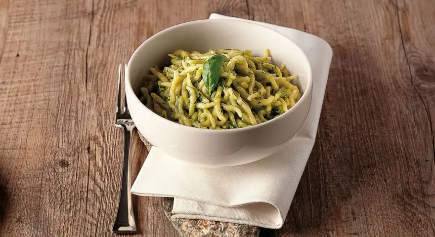 Un piatto invitante di trofie al pesto, guarnito con una foglia di basilico, su un tavolo di legno rustico.
