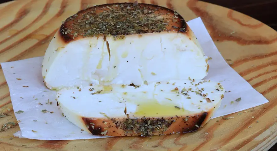 Ricotta al forno dorata e profumata con erbe aromatiche, servita su un tagliere di legno.