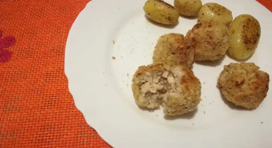 Piatto con polpette di pollo dorate e patate novelle condite. Una polpetta è stata aperta, mostrando l'interno succulento.