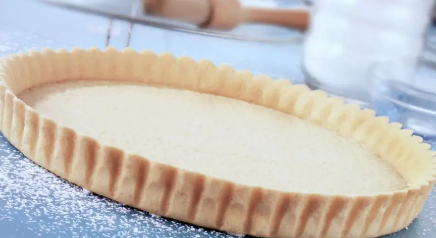 Base per crostata pronta, una deliziosa pasta frolla senza uova, cosparsa di zucchero a velo su un piano blu.