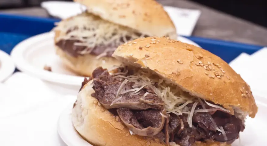 Panino con la milza, un classico street food siciliano, servito su un panino morbido con semi di sesamo e abbondante formaggio grattugiato.