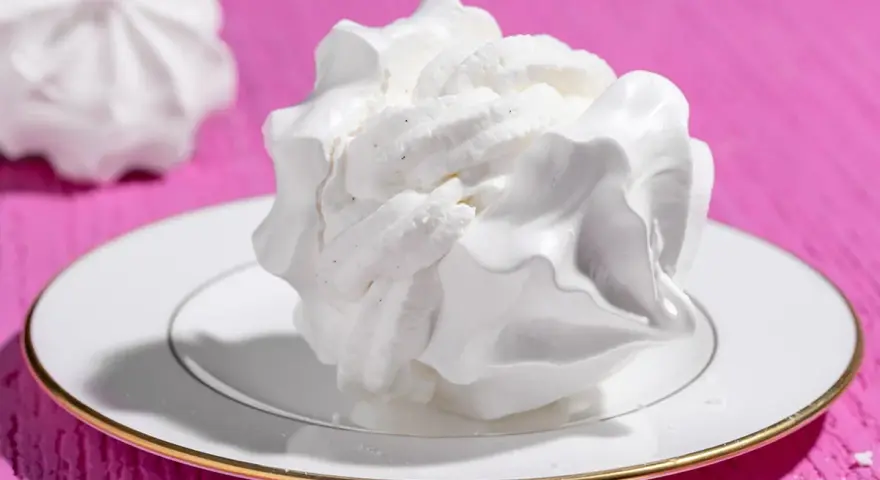 Dolci meringhe bianche, perfette per le tue ricette con albumi, su un piatto con bordo dorato, su sfondo fucsia.