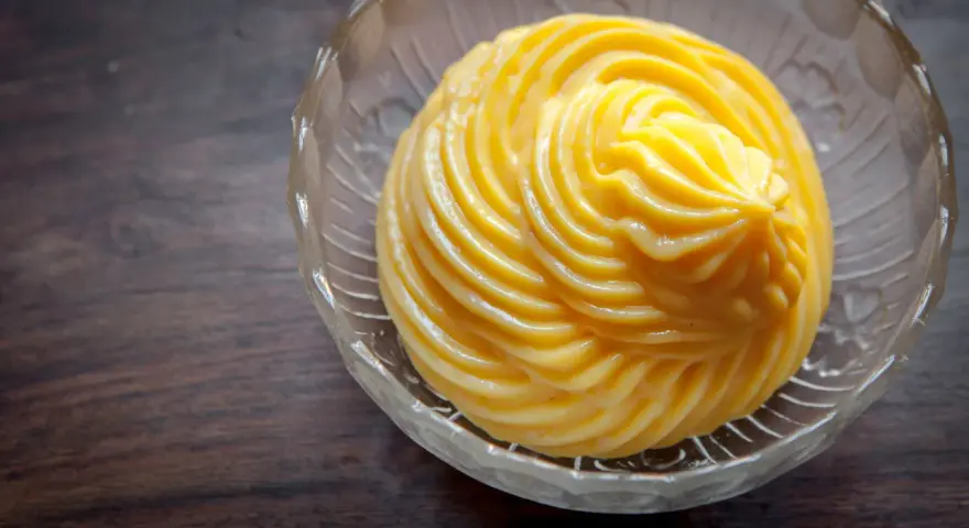 Crema pasticcera ricetta: una deliziosa crema gialla, liscia e lucida, servita in una ciotola di vetro trasparente con decori.