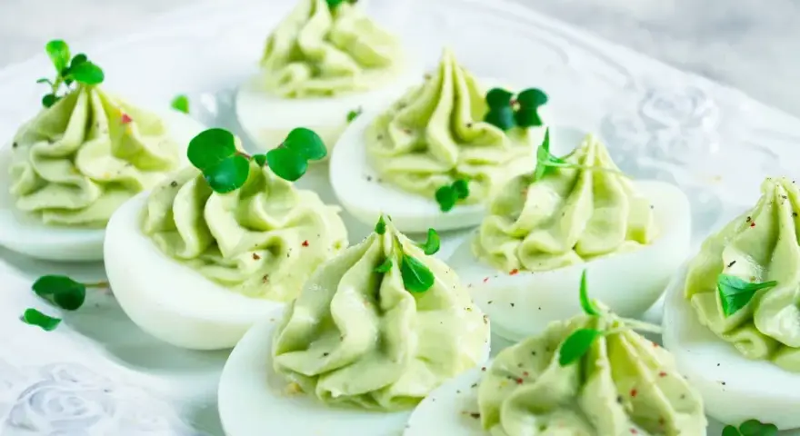 Uova ripiene per Pasqua, guarnite con crema verde e germogli freschi, un antipasto colorato e delizioso.