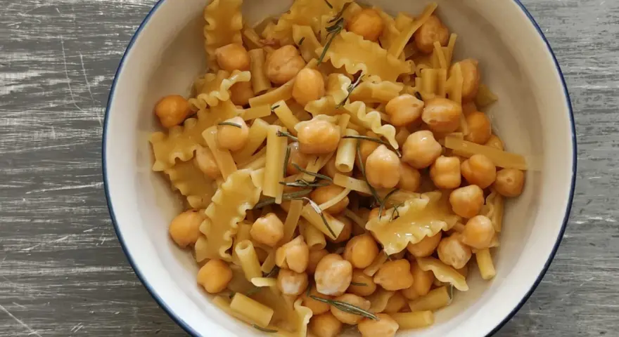 Un piatto invitante di pasta e ceci, con pasta corta e ceci dorati, guarnito con rosmarino fresco.