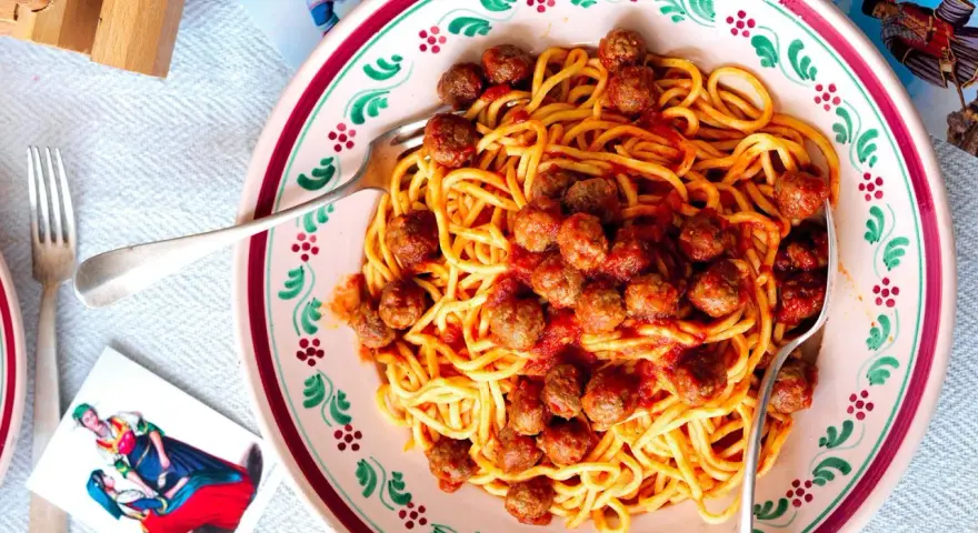 Un piatto di spaghetti alla chitarra con polpettine al sugo, serviti in un piatto decorato.