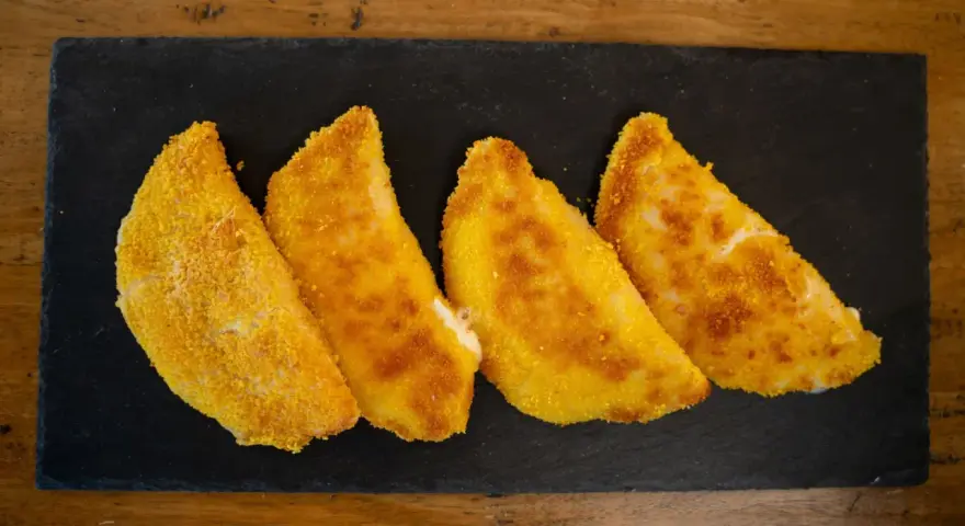 Quattro sofficini fatti in casa, dorati e croccanti, serviti su una pietra nera.