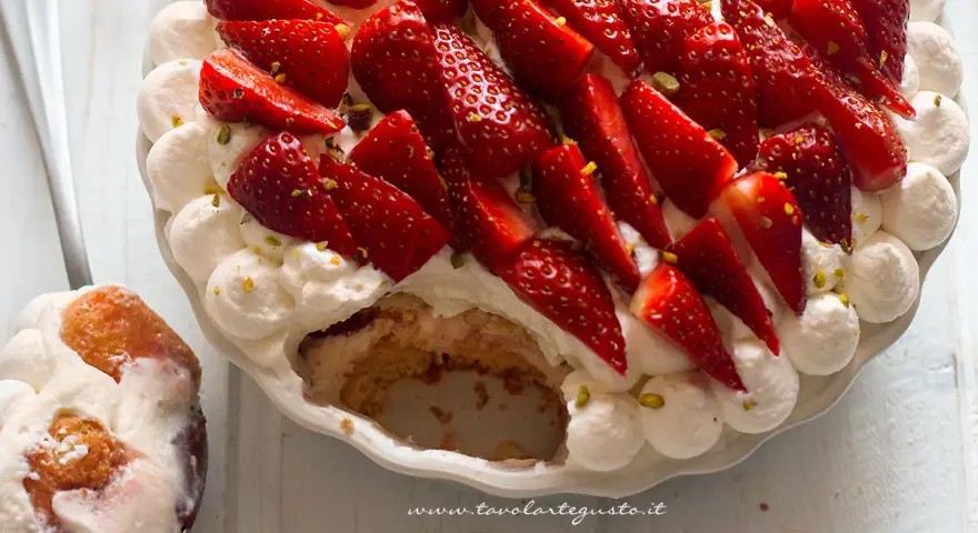 Delizioso tiramisù alle fragole, con panna montata, fragole fresche e pistacchi. Una fetta è già servita su un cucchiaio.