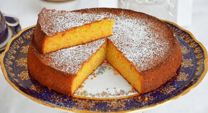Deliziosa torta carote e mandorle, spolverata di zucchero a velo, servita su un elegante alzata.