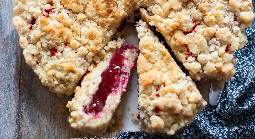 Torta con marmellata, con crosta friabile e ripieno rosso brillante. Una fetta mostra la consistenza succosa.