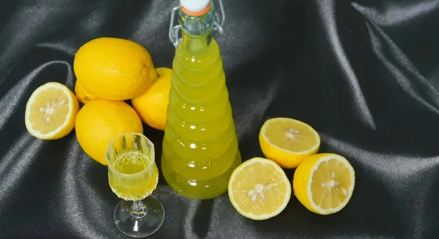 Limoncello fatto in casa: una bottiglia e un bicchierino di liquore giallo brillante, circondati da limoni freschi. La ricetta limoncello 1 litro alcool è pronta per essere gustata.