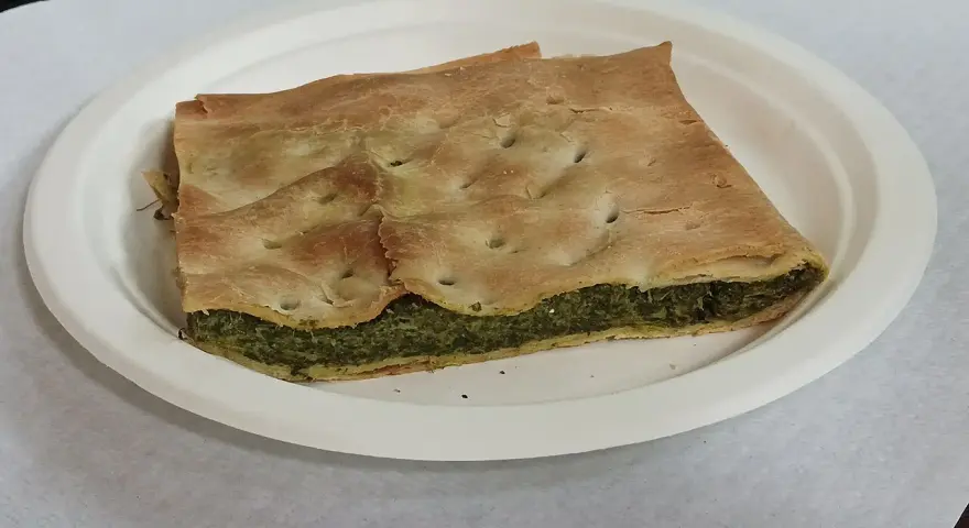 Una fetta di torta pasqualina originale genovese, con pasta sfoglia dorata e ripieno verde di spinaci e ricotta, servita su un piatto bianco.