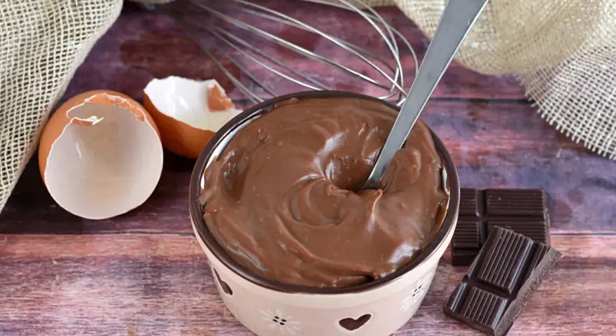 Crema pasticcera al cioccolato, liscia e invitante, pronta per essere gustata. Uova, frusta e cioccolato, ingredienti per un dolce momento.