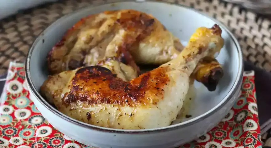 Cosce di pollo in padella, dorate e succulente, servite in una ciotola su un tovagliolo decorato.