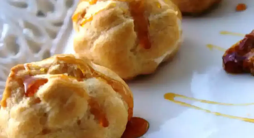 Bignè alla crema soffici e dorati, bagnati da un filo di caramello lucido su un piatto bianco.