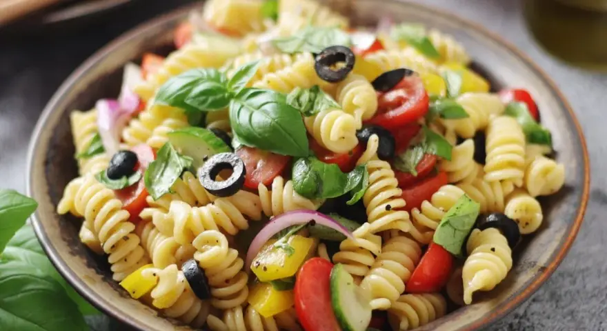 Un piatto invitante di insalata di pasta con fusilli, pomodorini, olive nere, cipolla rossa, cetrioli e basilico fresco.