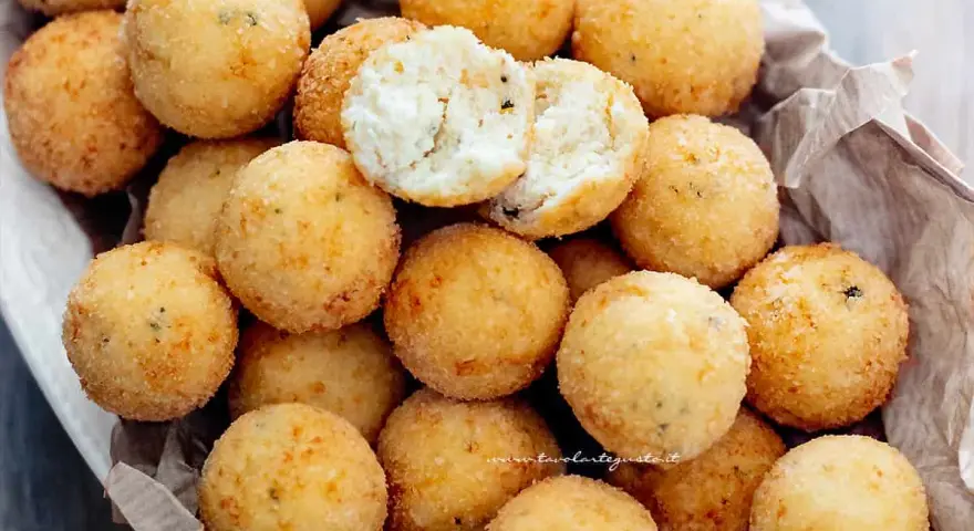 Un cesto pieno di croccanti polpette di ricotta, dorate e invitanti. Una è aperta, mostrando il morbido interno.