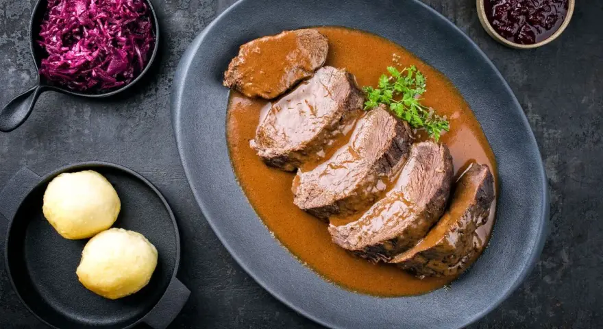 Fette fette di girello di vitello in salsa, accompagnate da cavolo rosso e canederli.